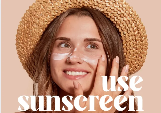 Woman wearing a straw hat applying sunscreen to her face.